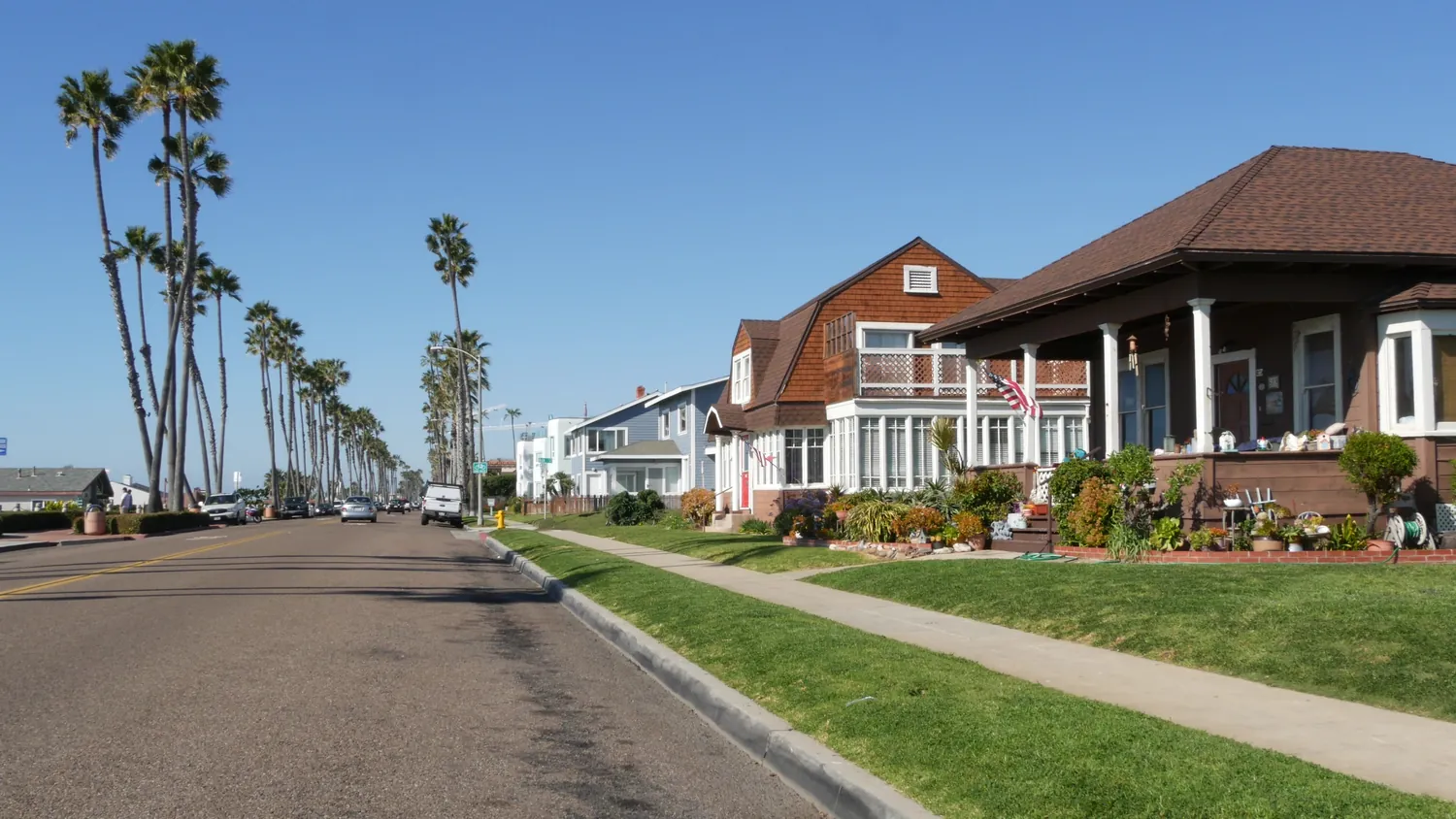 Suburban street with palm trees, colorful houses, and a clear blue sky. The scene is peaceful and sunny, conveying a warm, inviting atmosphere.